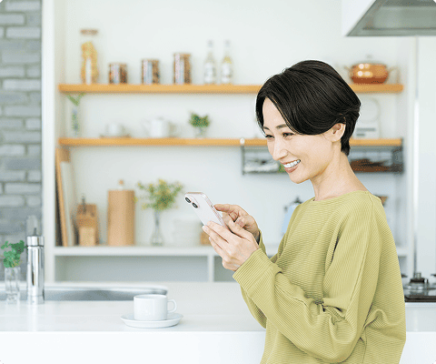 キッチンでスマートフォンから住まいの設備を操作する女性